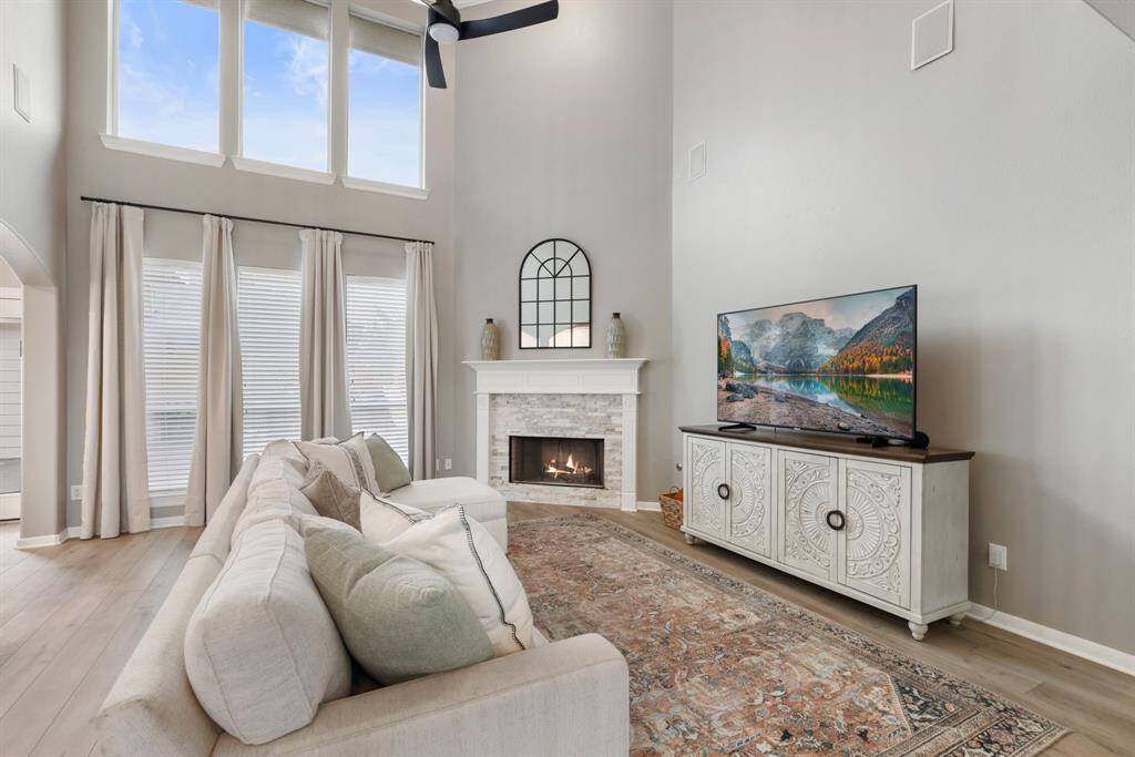 This spacious living room features a high ceiling with large windows for natural light, a cozy fireplace, and elegant decor.