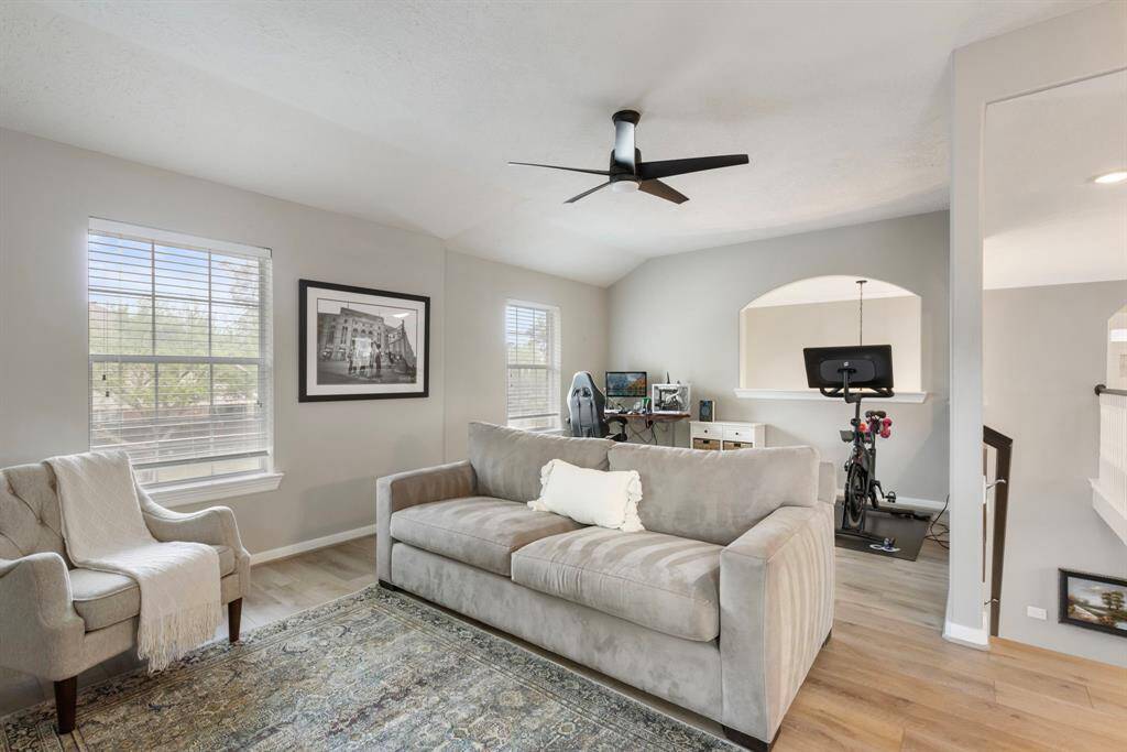 Bright and airy living space with light wood floors and neutral walls. Features a cozy seating area, modern ceiling fan. Large windows provide ample natural light, creating an inviting atmosphere.