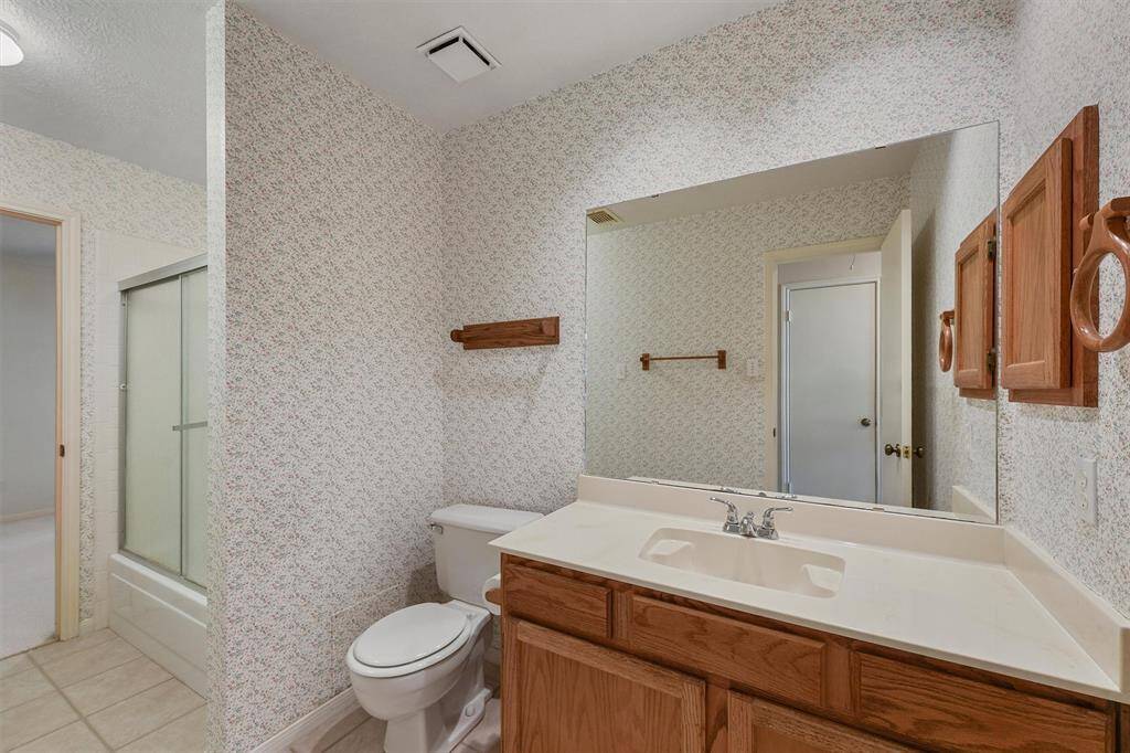 Secondary bathroom features a large mirror, wooden cabinetry, and a shower-tub combo. It connects to one of the secondary bedrooms.