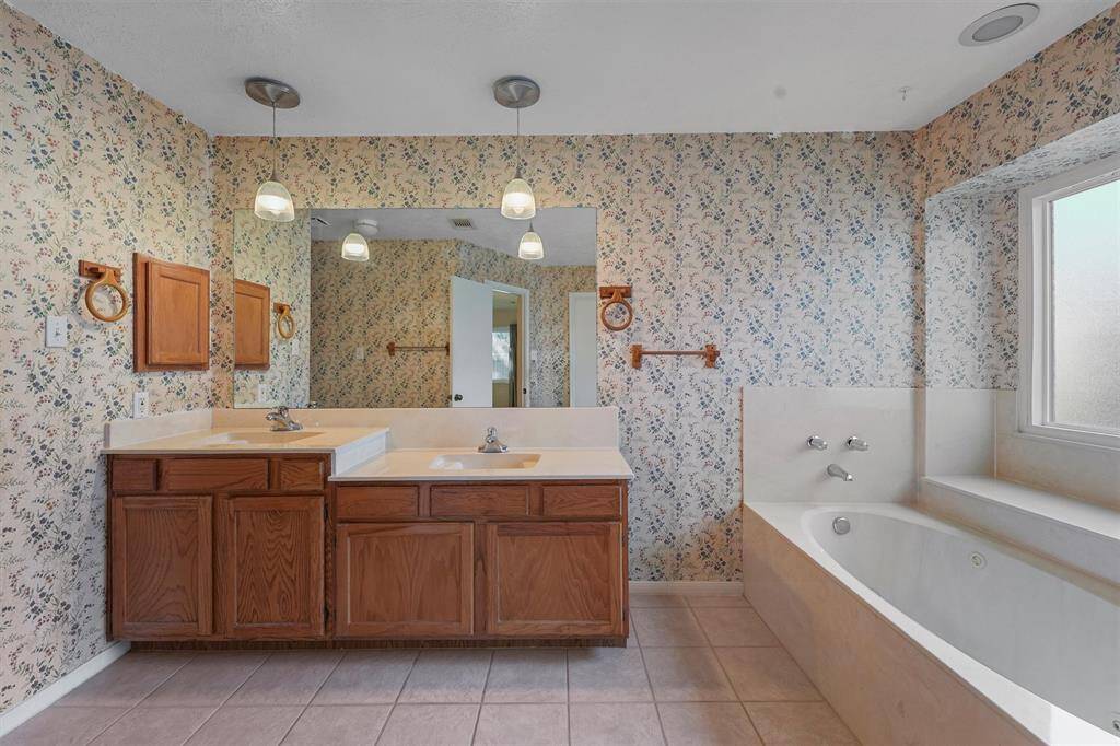 The primary bathroom features a dual-sink vanity with wooden cabinets, and a large mirror. The space is illuminated by pendant lights, creating a cozy atmosphere.