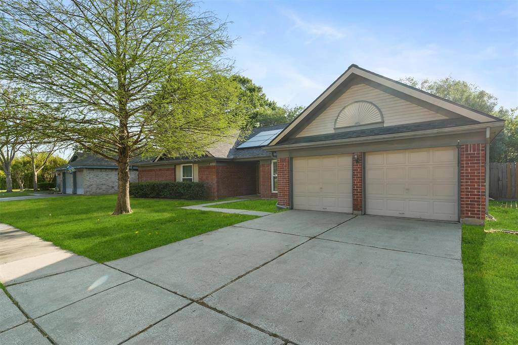 The home features a classic brick exterior with a double garage. It has a spacious driveway and a well-maintained lawn with mature trees, offering excellent curb appeal.
