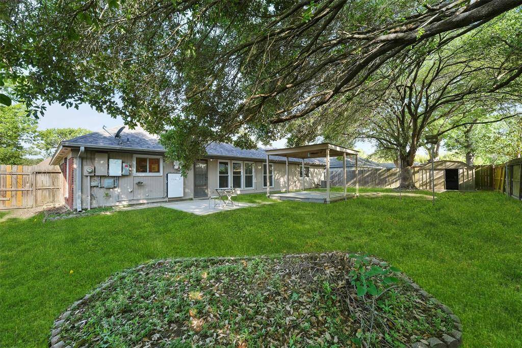 Experience serene outdoor living with a shaded backyard under mature trees, featuring a Tesla Powerwall for energy efficiency.
