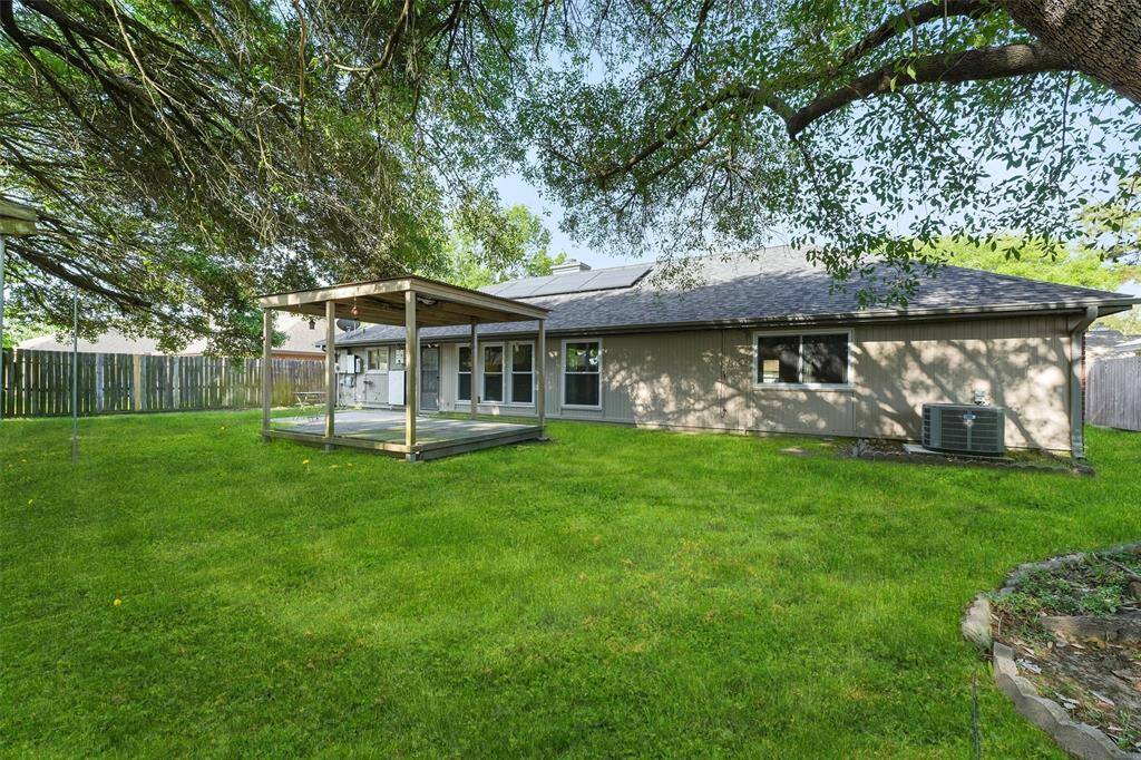 This backyard features a spacious lawn and includes a covered patio, ideal for outdoor gatherings, and is enclosed by a privacy fence.
