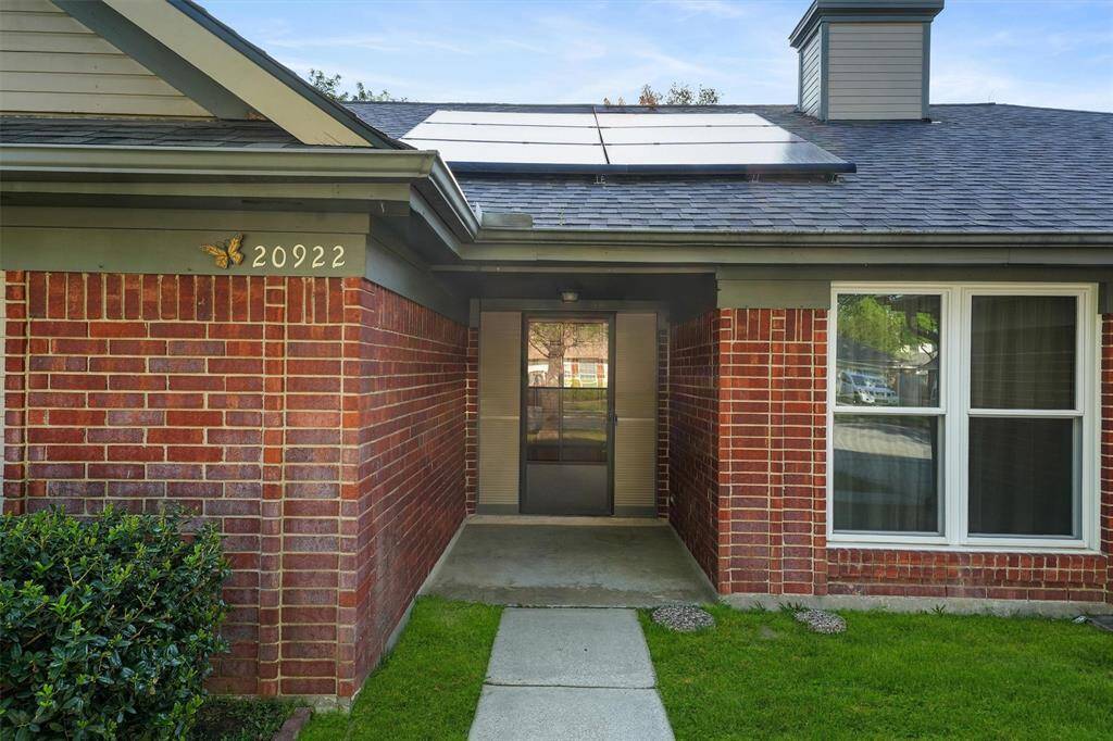 The pathway leads to a covered front porch. The house features solar panels on the roof and double pane windows throughout, offering a modern and energy-efficient design.