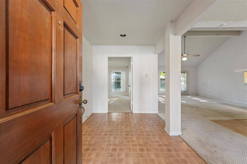 The entryway opens into a spacious interior. The area features a tiled foyer leading to the living room with high ceilings and a ceiling fan, offering plenty of natural light through large windows.