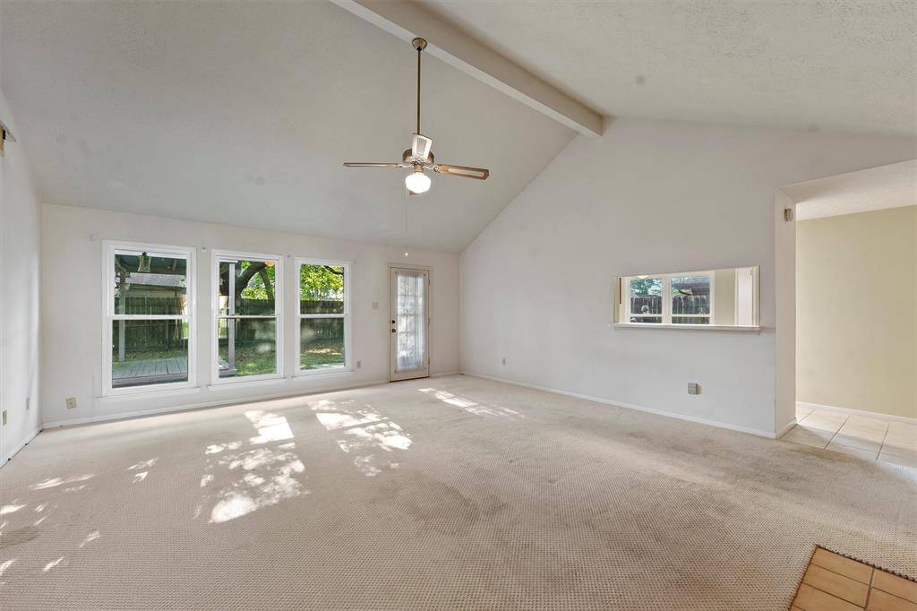 Bright and spacious living room with high vaulted ceiling and a ceiling fan. A passthrough window connects to the kitchen, enhancing the open feel.