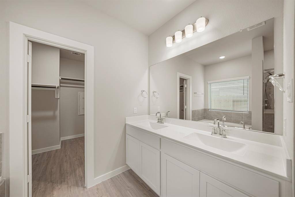 It features double sinks, granite countertops and backsplash, a large mirror, and vinyl floors.