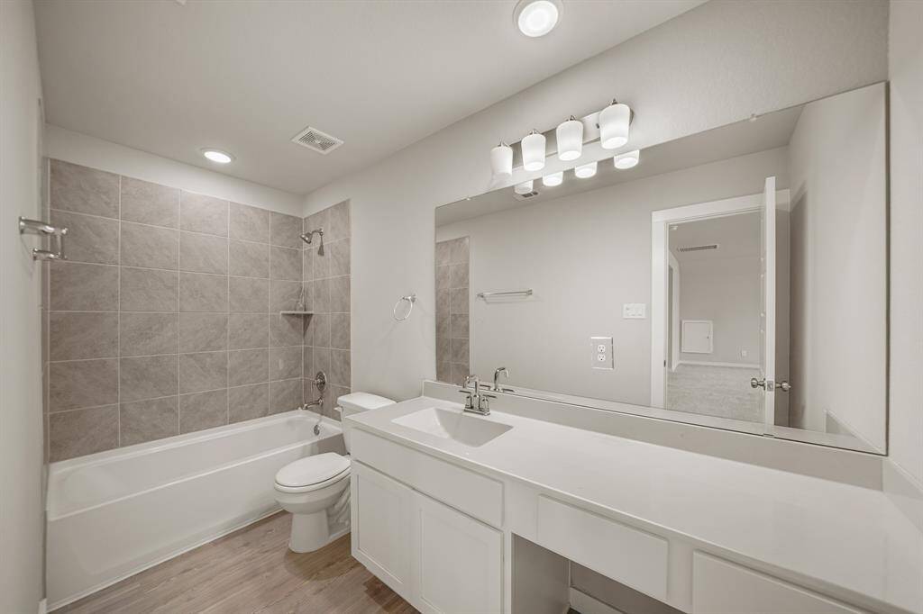 Secondary bathroom with vinyl floors, a vanity area, granite countertops, a large mirror, recessed lighting, and a shower/tub combo.