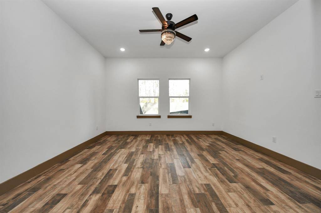 This primary room features wood-look flooring, neutral walls, and recessed lighting. It includes a ceiling fan and two windows for natural light