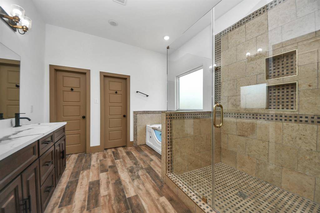This bathroom features a spacious glass-enclosed shower with elegant tile work, a luxurious bathtub, and a dual-sink vanity with a marble countertop. The room is accented with wood-look flooring and modern fixtures.