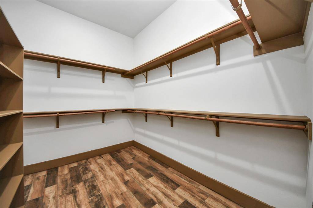Primary walk-in closet with multiple wooden shelves and hanging rods