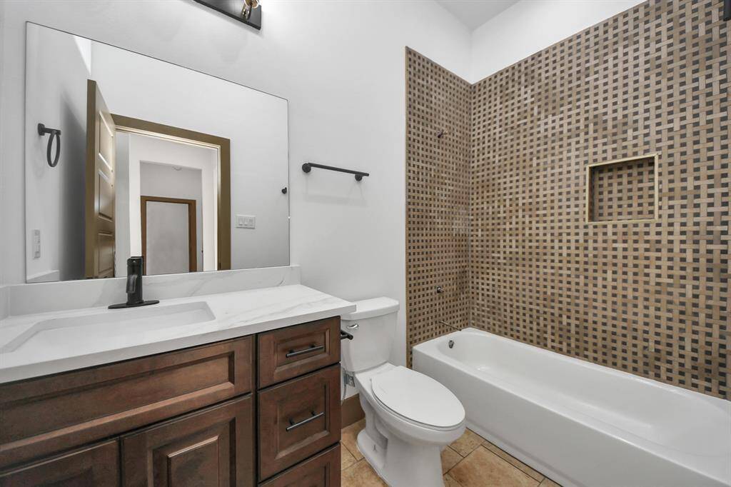 This bathroom features a modern design with a dark wood vanity, white countertop, and a sleek black faucet. The tub-shower combo is accented with a stylish woven tile pattern