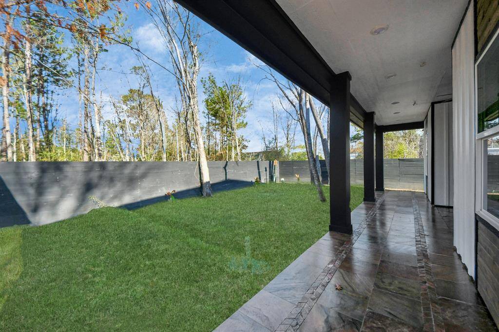 Covered patio with a tiled floor, overlooking a spacious, fenced backyard with lush grass and trees
