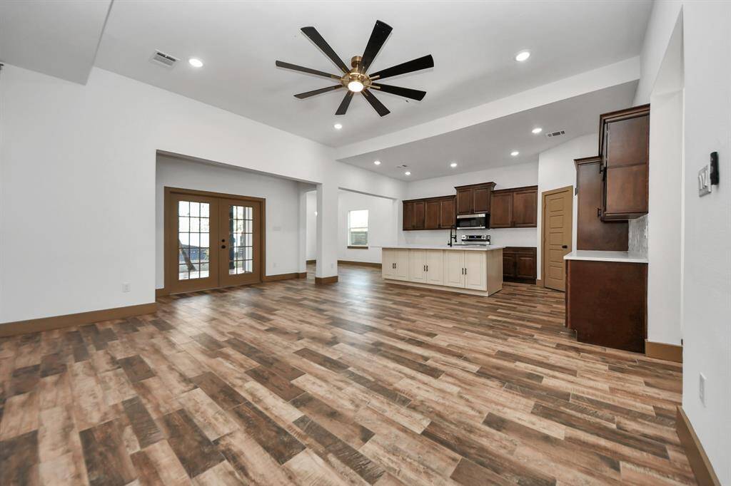 This spacious kitchen features elegant dark wood cabinets, a large contrasting island, and modern stainless steel appliances. It has wood-look tile flooring and recessed lighting