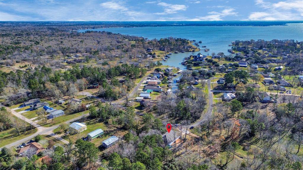 This aerial view showcases a peaceful lakeside community with the home marked by a red pin. The area is surrounded by lush greenery and offers close proximity to the water, ideal for those seeking a tranquil lifestyle with scenic views and outdoor activities.
