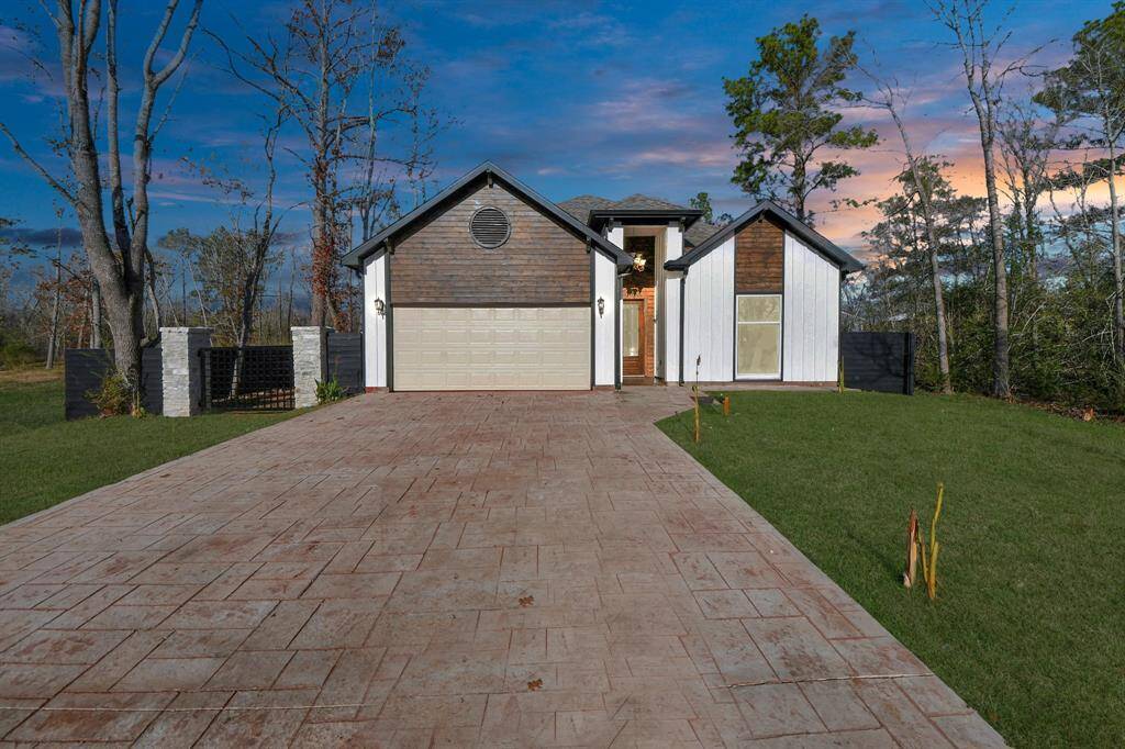 Modern home with a mixed-material facade, including wood and white siding. It has a spacious stamped concrete driveway and is surrounded with mature trees.