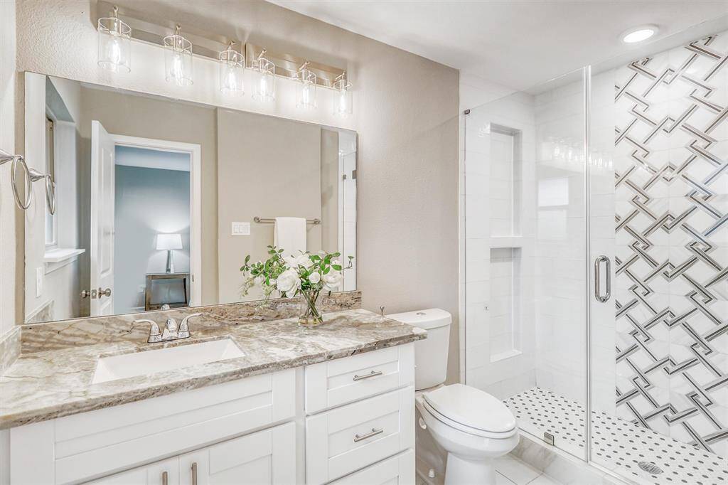 The ensuite bath features a granite-topped vanity with ample storage, modern lighting, and a glass-enclosed walk-in shower with designer tile accents.