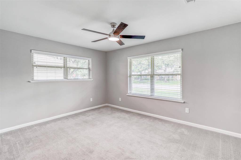 This spacious second bedroom offers plush carpet, a modern ceiling fan, and large windows that fill the room with natural light—an ideal space for guests or family.