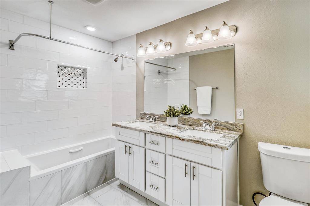 This beautifully updated guest bathroom features a dual-sink vanity with marble-look countertops, stylish lighting, and a fully tiled tub/shower combo with a designer accent niche.