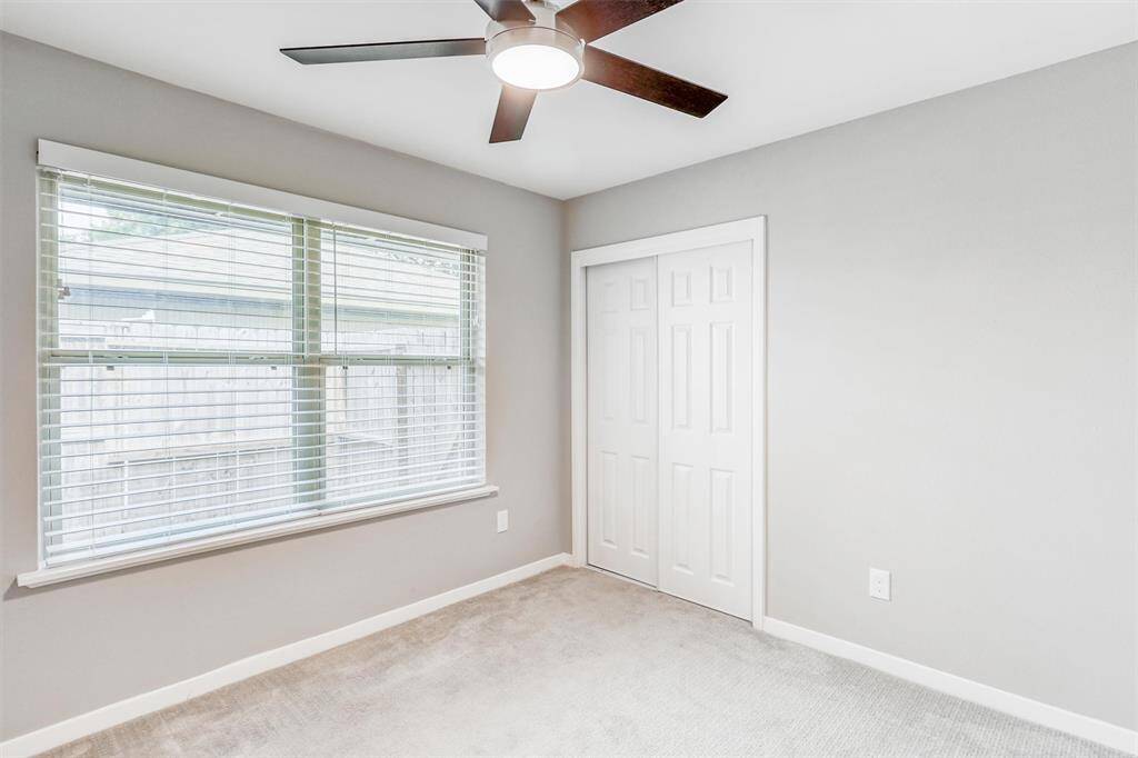 Bright and inviting, this third bedroom offers fresh neutral paint, soft carpet, a modern ceiling fan, and a wide window that fills the space with natural light.