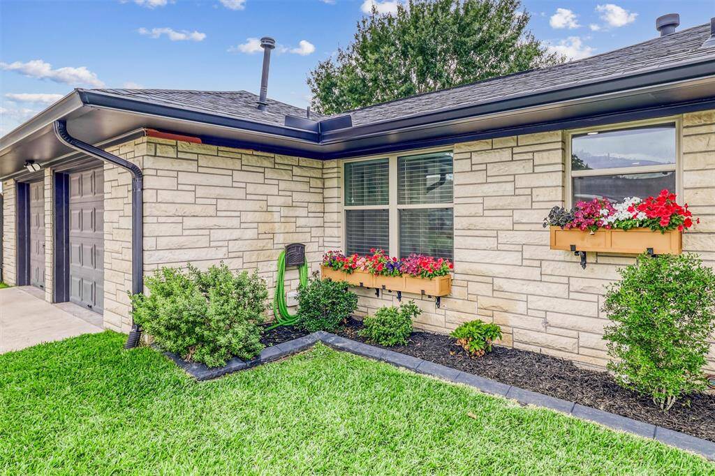 Window flower boxes and fresh paint complement the home’s timeless stone exterior, adding a touch of charm to the modern design.