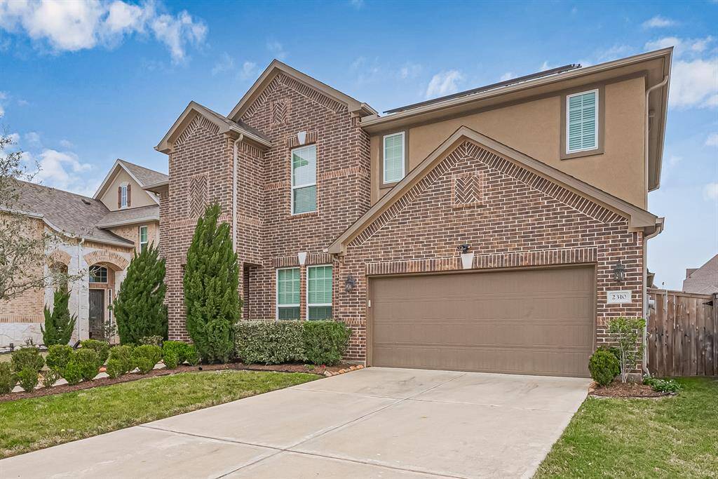 A tasteful brown brick facade sets a timeless tone, complemented by a long, smooth driveway leading to the attached two-car garage. Manicured landscaping enhances the curb appeal, with neatly trimmed bushes lining the walkway to the front entrance. The expansive front lawn adds to the grand presence of the home.
