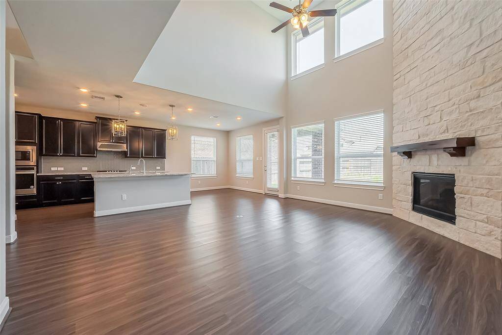 Designed for both comfort and connection, this spacious living area seamlessly flows into the kitchen, creating an effortless open-concept design. Oversized windows span two levels, allowing sunlight to flood the space, while soaring ceilings enhance the sense of openness. A striking fireplace set against a tall accent wall adds warmth and architectural interest, making this a perfect gathering space.