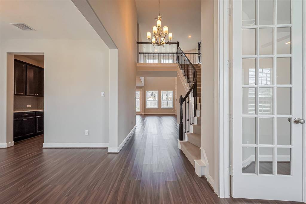 A striking first impression, this view showcases the home's grand staircase ascending to the right, leading to the open upstairs landing. Beyond, the living room unfolds in the distance, framed by soaring ceilings and expansive windows. A statement chandelier casts a warm glow, tying the space together.