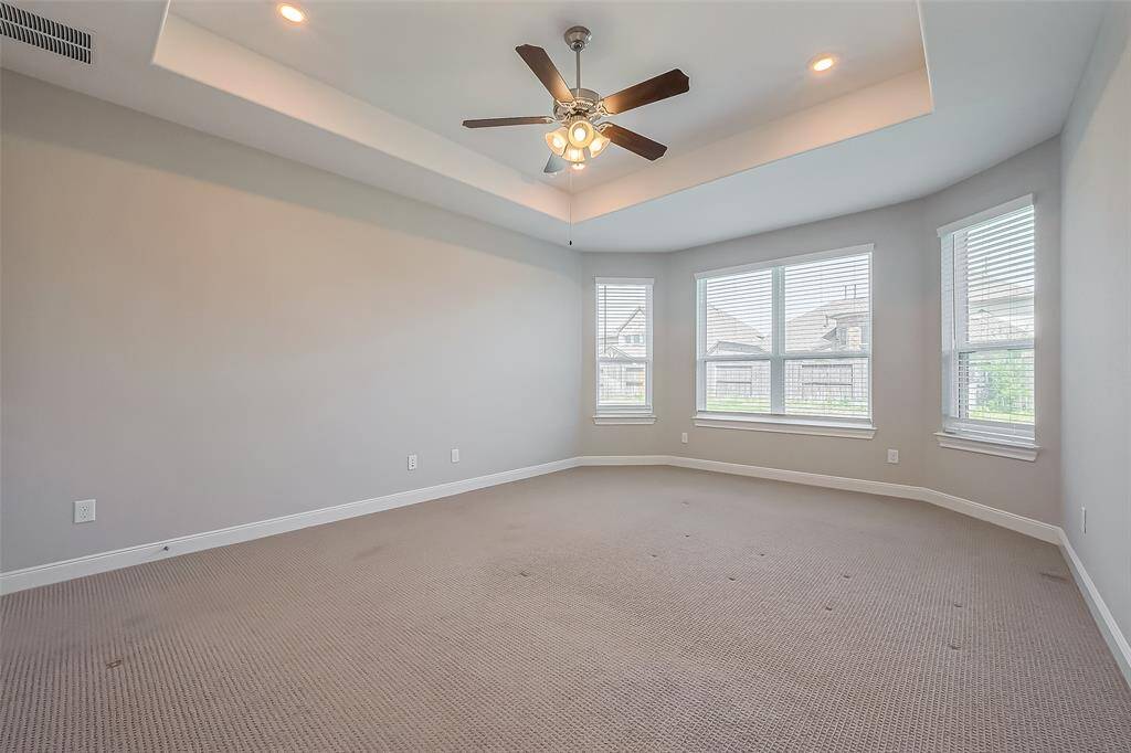 The primary bedroom is an expansive retreat featuring plush carpeting and a recessed ceiling with soft lighting. Large windows invite in natural light, while a ceiling fan enhances comfort. Double doors lead to the en suite, offering a seamless connection to the luxurious bath space.