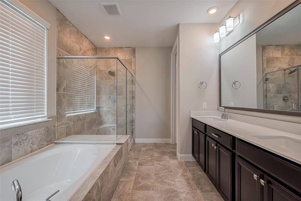 Thoughtfully designed, this en suite bath includes an extended dual-sink vanity with ample under-storage, a full-width mirror, and stylish lighting. The beautifully tiled space features a soaking tub beside a separate glass-enclosed shower with a built-in bench, offering both relaxation and convenience.