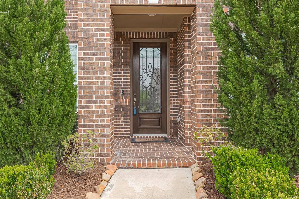 A closer look at the main entrance shows the intricate brickwork, highlighting the craftsmanship of the exterior. The covered recessed entryway, framed by lush greenery, offers a welcoming transition into the home.