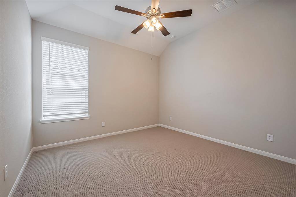 A generously sized room with a high ceiling, plush carpeting, and a ceiling fan with a built-in light fixture. A large window brightens the space, creating an inviting atmosphere.