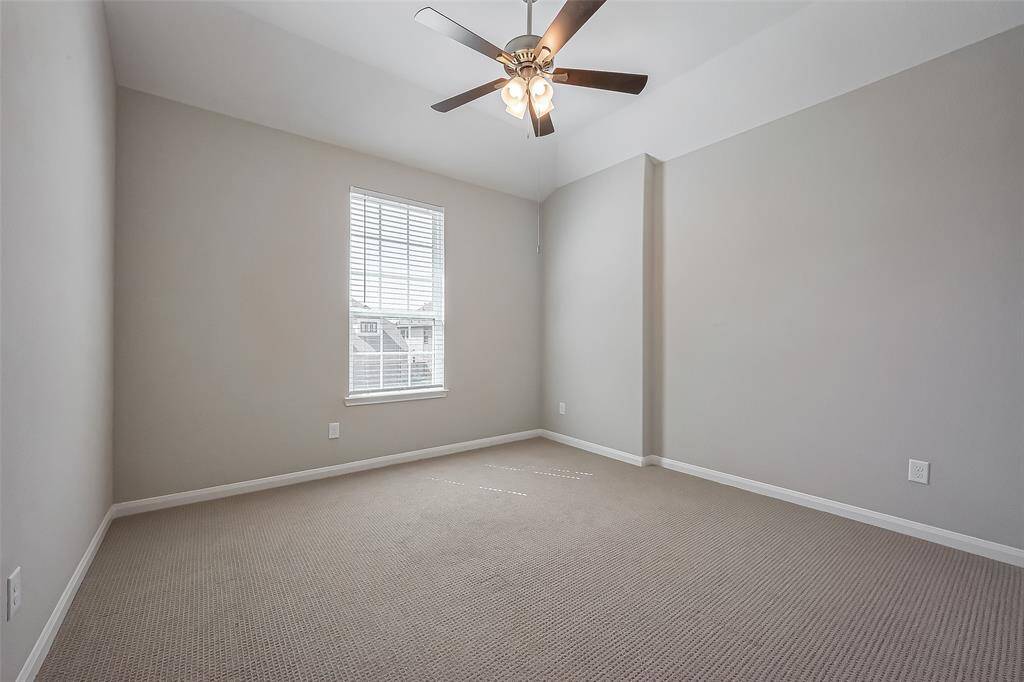 Spacious and bright, this room features a large window, soft carpeting, and a ceiling fan with a light fixture. The high ceiling adds to the airy feel, making it a comfortable retreat.