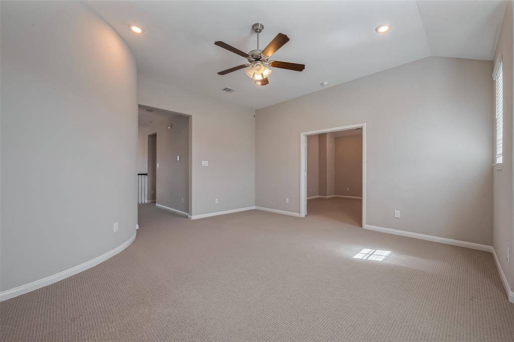 A versatile and expansive space designed for entertainment and leisure. Plush carpeting, recessed lighting, and a ceiling fan create a comfortable environment, while large windows provide plenty of sunlight. The high ceiling enhances the open feel.