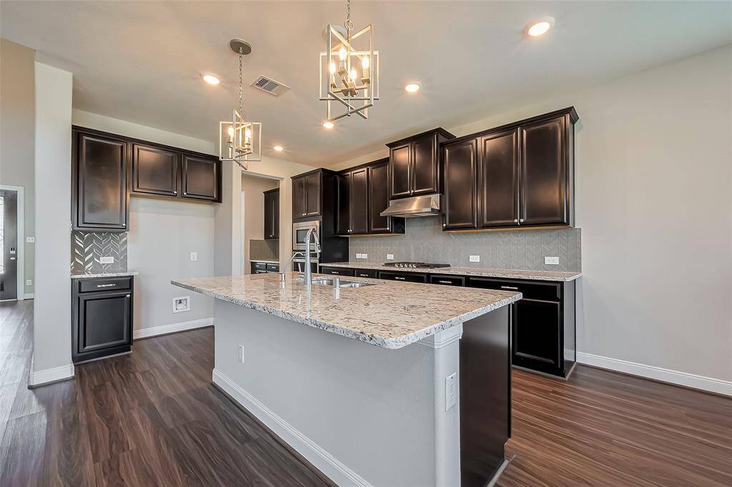 Expansive and thoughtfully designed, this kitchen features rich wooden cabinetry, both overhead and below, offering ample storage. Sleek granite countertops stretch across the space, complemented by a large center island with sophisticated pendant lighting. Recessed lighting highlights the contrast between the dark cabinets and lighter elements, while the adjacent breakfast area ensures a seamless flow for casual dining.