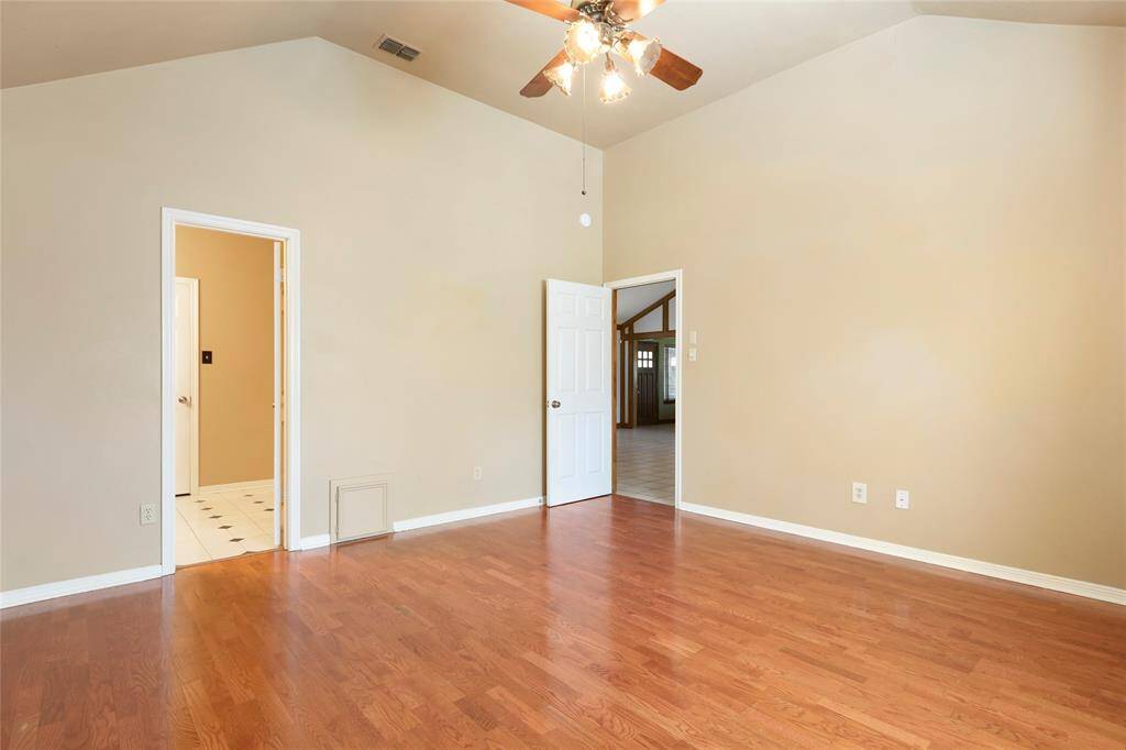 Spacious primary bedroom with wood floors and high ceiling.