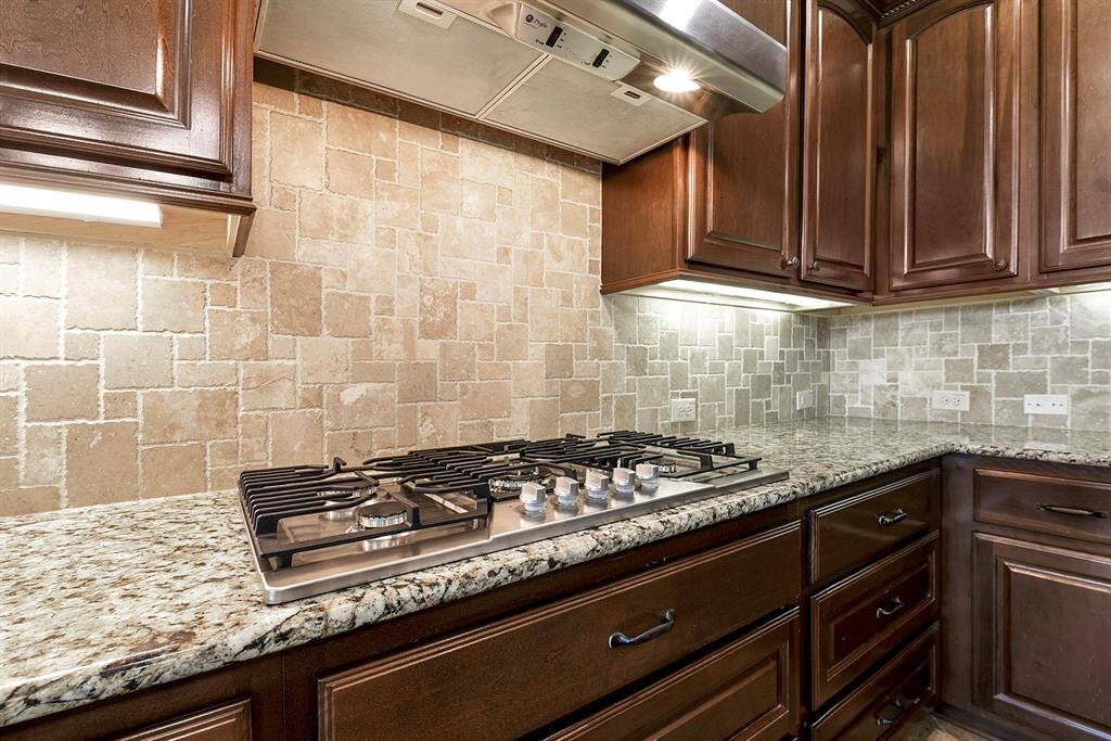 This kitchen is fully equipped with endless drawer space for added convenience, a tile stone backsplash, and a five-burner gas stove. Undermount lighting highlights the beauty of the countertops and adds a warm ambiance to the space.