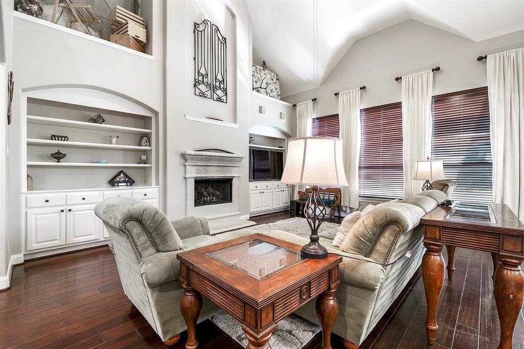 Another view of this spacious living room highlights the gas fireplace nestled between the built-in storage and display nooks, serving as a stunning focal point. The wall of back windows provides a beautiful view of the backyard, flooding the room with natural light and seamlessly connecting the interior to the outdoors.
