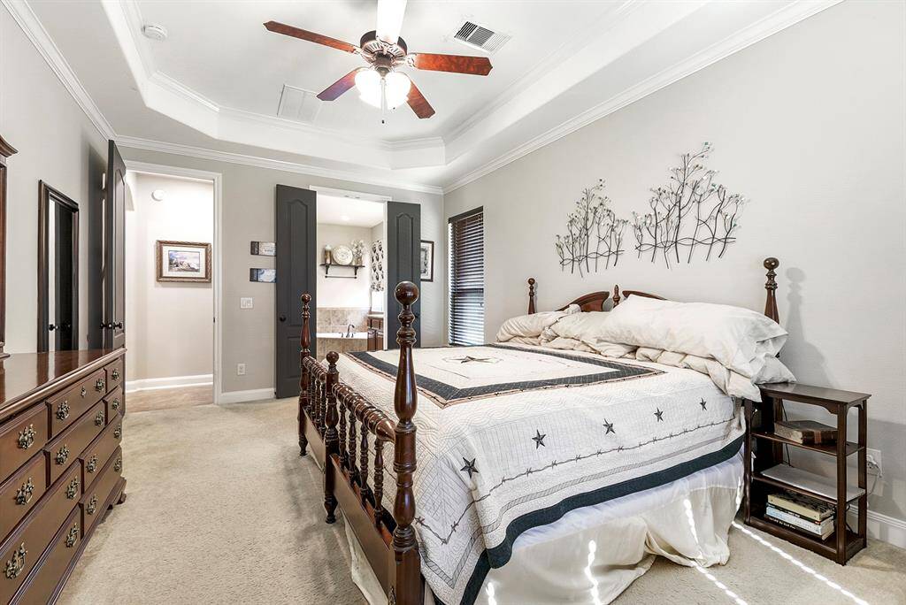 Another view of the primary en suite showcases high ceilings with a drop-down ceiling fan, adding a touch of elegance. The trey ceiling is highlighted by double crown molding, creating a sophisticated atmosphere. Double doors lead into the luxurious attached en suite bath, while a large wardrobe closet provides ample storage space.