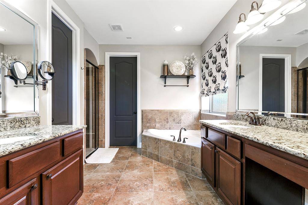 This luxurious bathroom offers plenty of space, featuring dual vanities with sinks, including one with a convenient prep vanity. The soaking tub provides a relaxing retreat, while the large glass and tile walk-in shower includes a built-in seating bench. Additionally, the huge wardrobe closet offers ample storage for all your essentials.
