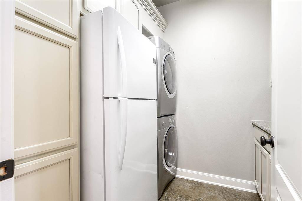The large utility room offers ample space for a full-size washer and dryer, as well as an extra refrigerator/freezer. Built-in cabinetry on both sides, along with countertop space, provides plenty of room for folding clothes or prepping, making laundry tasks more efficient and organized.