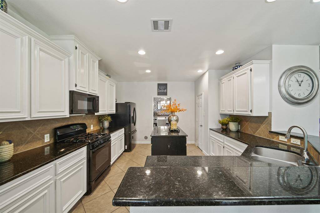 White cabinetry, granite countertops, and tile flooring create a crisp, clean aesthetic, complemented by recessed lighting and a classic backsplash.