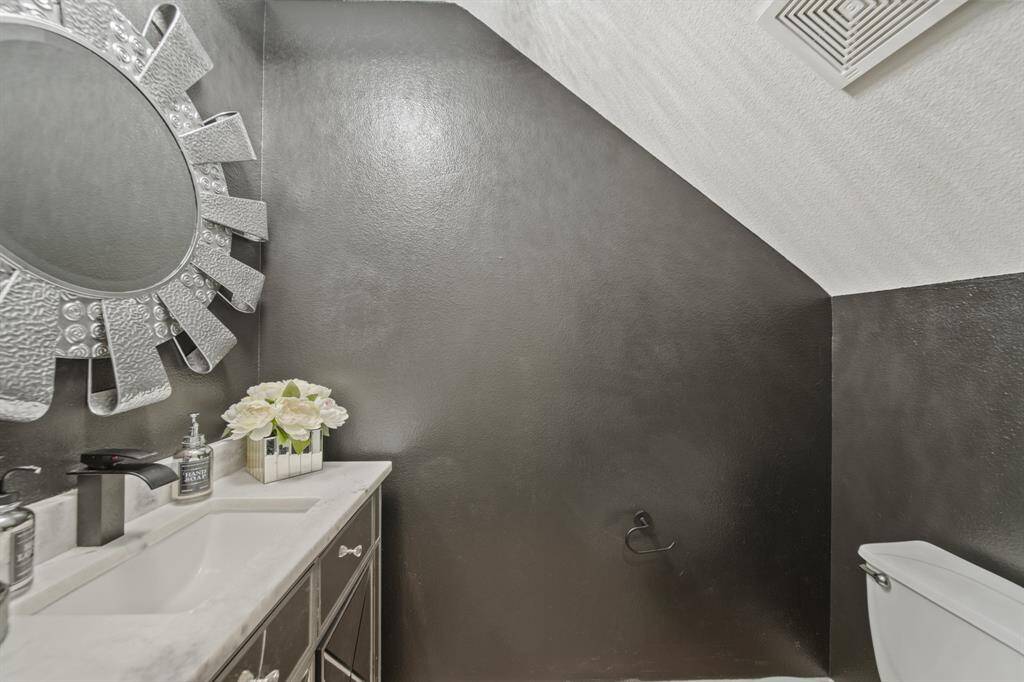 The elegant half bath features a dramatic accent wall, a mirrored vanity with marble countertop, and modern lighting, offering a touch of glam for your guests.