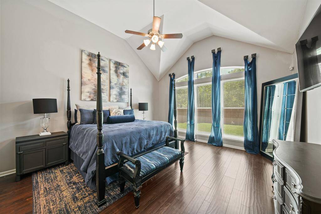 Bask in the serene beauty of the spacious primary retreat, featuring a dramatic vaulted ceiling, rich wood flooring, and a wall of windows that fill the space with natural light.