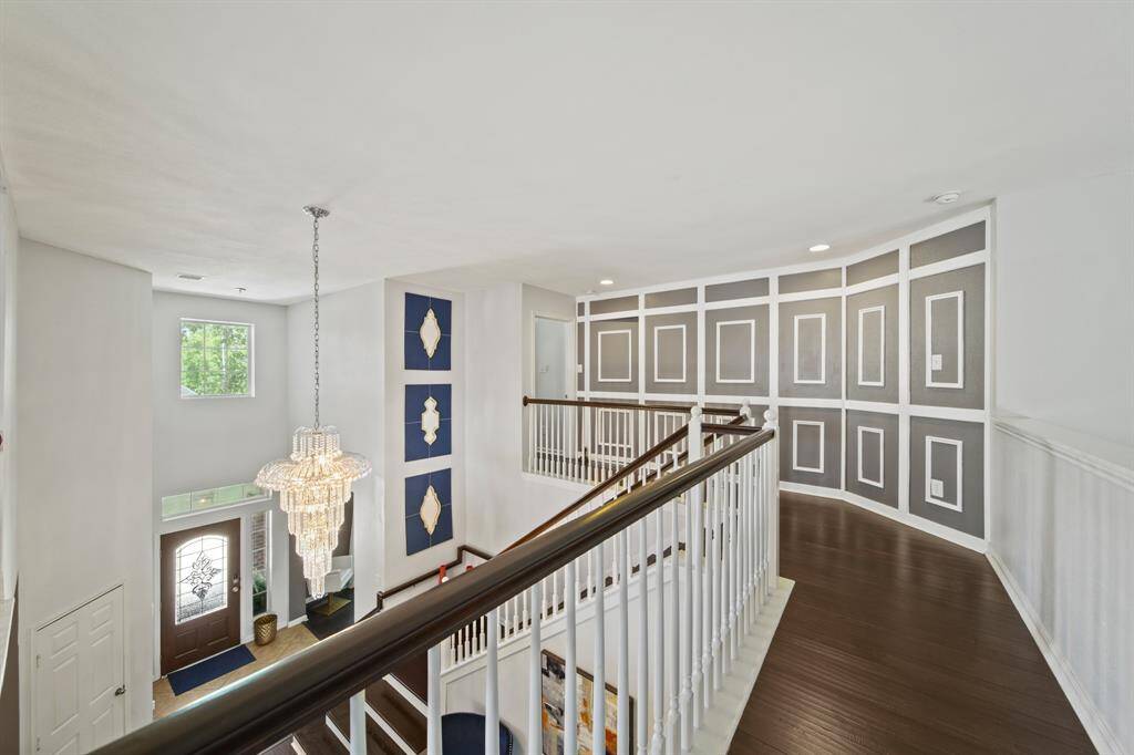 A striking view from the upstairs landing showcases custom accent wall panels and a sparkling crystal chandelier above the elegant foyer below.