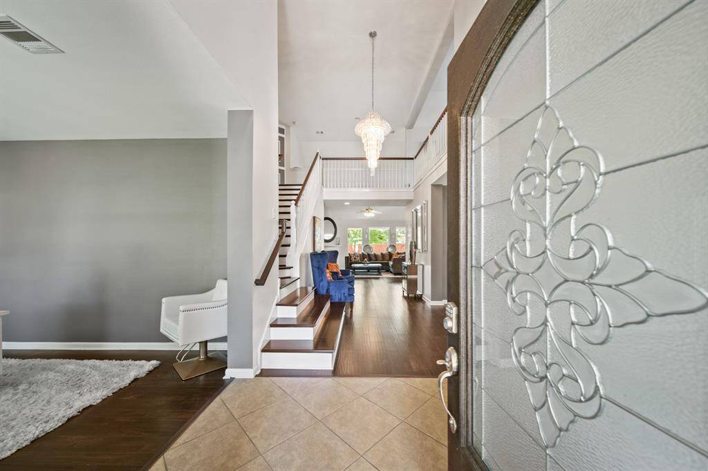 Step through the elegant glass-paneled front door into a soaring two-story foyer with a dramatic chandelier, tile entry, and rich wood flooring that flows seamlessly throughout the main living areas.
