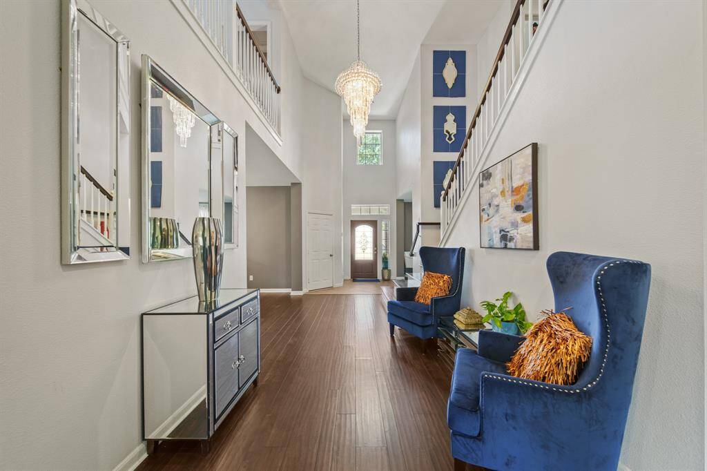 The spacious foyer boasts an open feel with high ceilings, crisp neutral tones, and beautiful architectural details, including a stunning light fixture and upper-level balcony view.
