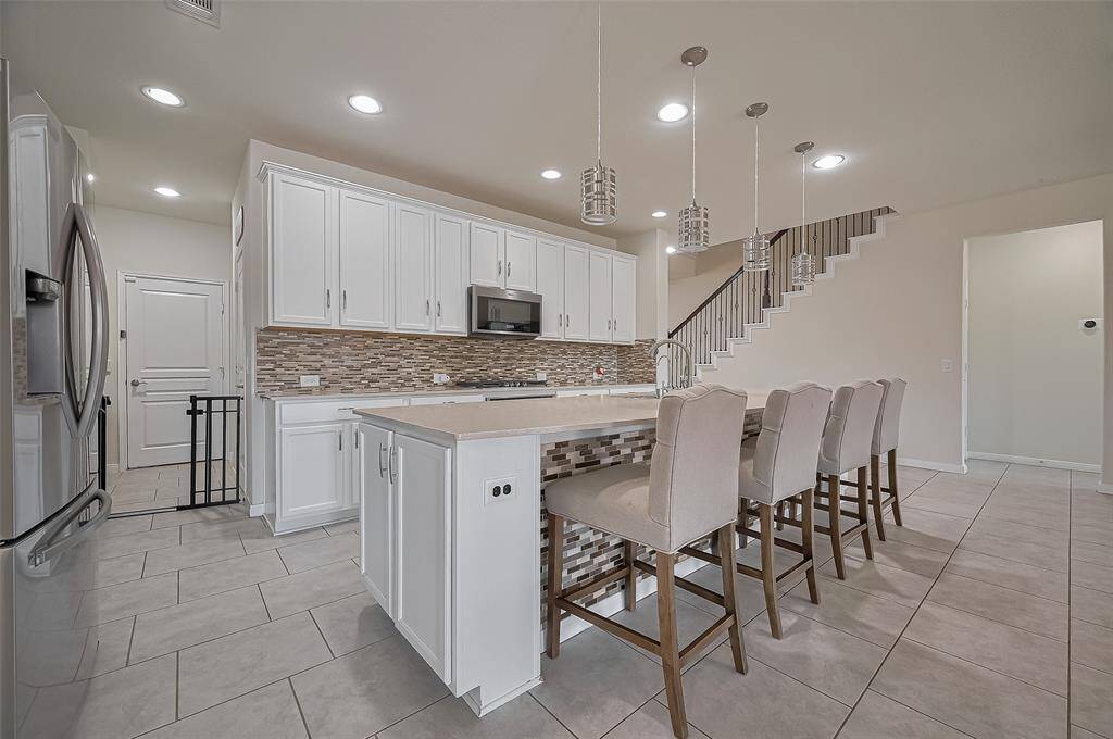 A chef’s dream—this kitchen is equipped with white cabinetry, a stylish mosaic tile backsplash, stainless steel appliances, and a gas cooktop. The long island provides ample seating and serves as a central gathering space.
