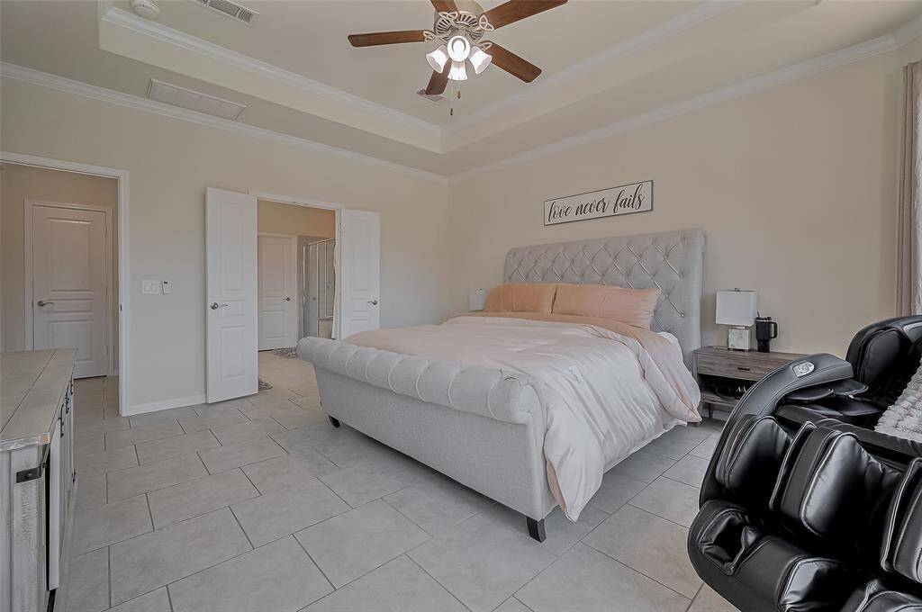 Alternate view of the primary suite. Tile flooring in a brick pattern makes for easy care. Tray ceiling with double crown molding for decorative accents. Double doors leads to the primary bathroom.