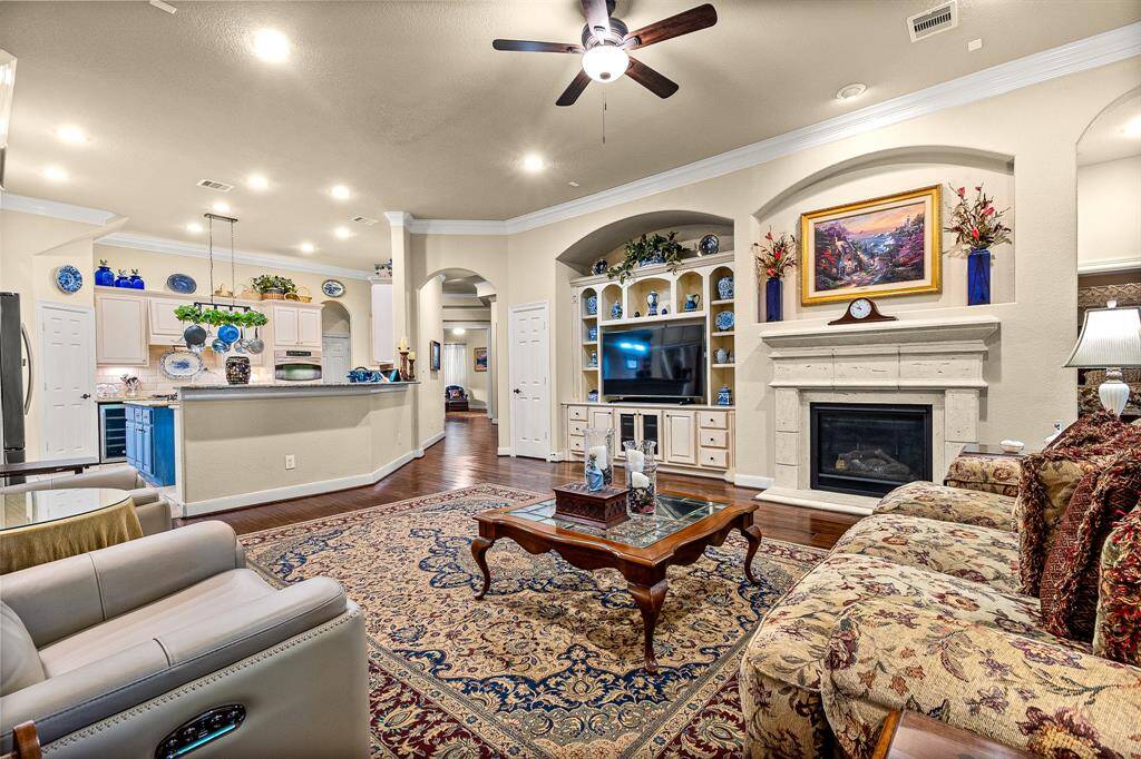 Notice the built in entertainment nich in the Living Room which features an open floor plan with elegant crown molding, a gas fireplace, and built-in shelving and storage. The room seamlessly connects to a kitchen with a breakfast bar, creating a perfect space for entertaining. Warm lighting and tasteful decor add to the home's charm.